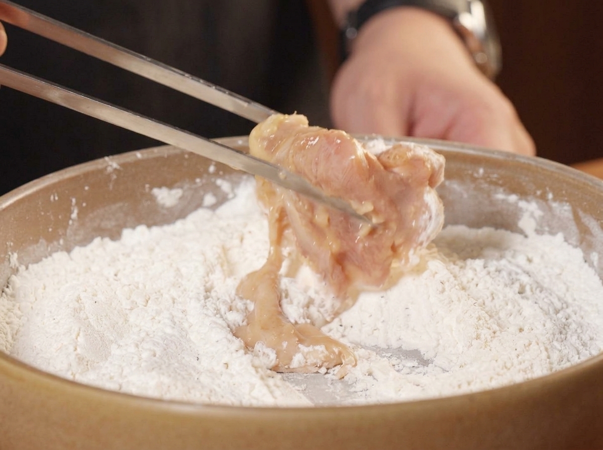 Pinzas metálicas colocando un trozo de pollo marinado húmedo en el plato con el rebozado seco.