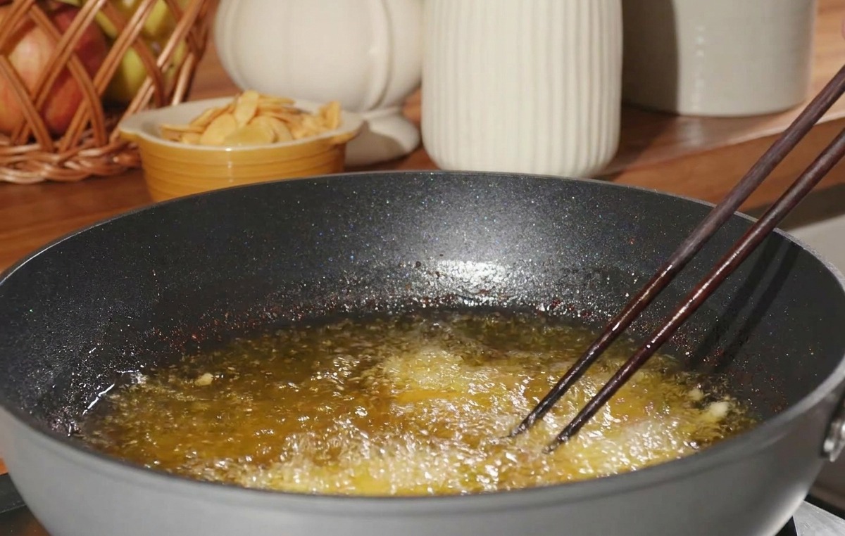 Un trozo de pollo rebozado entrando con cuidado con la ayuda de palillos en una sartén con aceite muy caliente.
