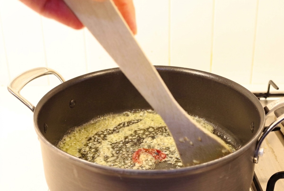 Ajo picado y chiles mezclándose con mantequilla derretida en una olla oscura con una espátula de madera.