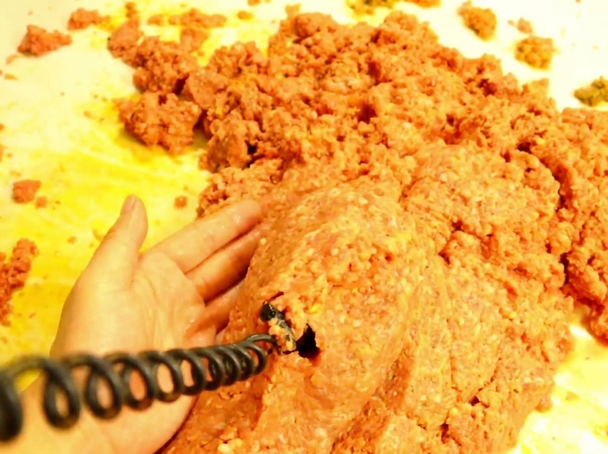 Una cuchara de madera sirviendo la mezcla de carne caliente sobre un pan de hamburguesa tostado.