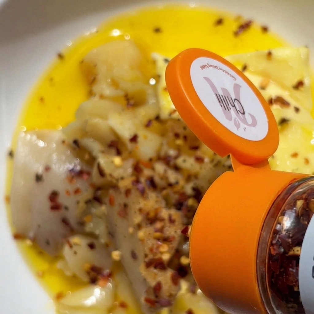 Copos de chile rojo cayendo desde un tarro de especias sobre un bol con ajo machacado y mantequilla.
