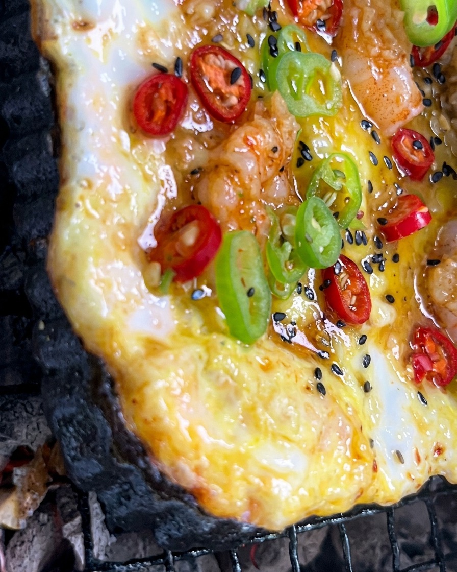 Salsa de ajo picado siendo pincelada sobre una colorida pizza que se cocina sobre fuego de carbón.