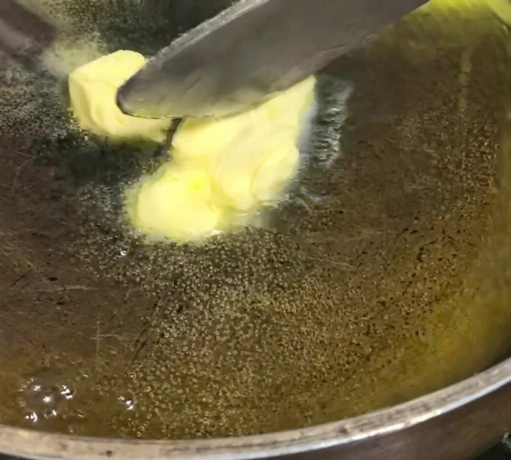 Cubos de mantequilla amarilla derritiéndose y burbujeando en una sartén oscura a fuego bajo.