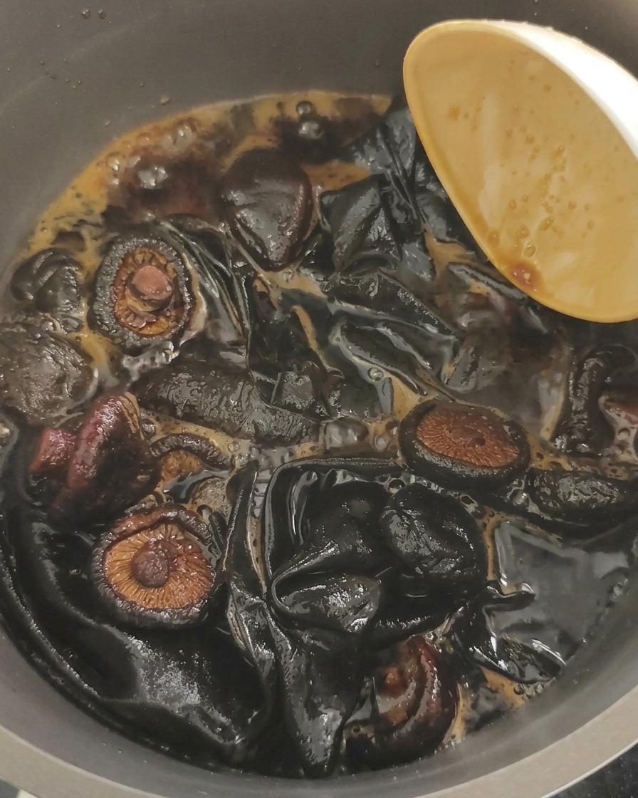 Primer plano de setas oreja de madera y trozos grandes de kombu cocinándose en un líquido oscuro de soja burbujeante.