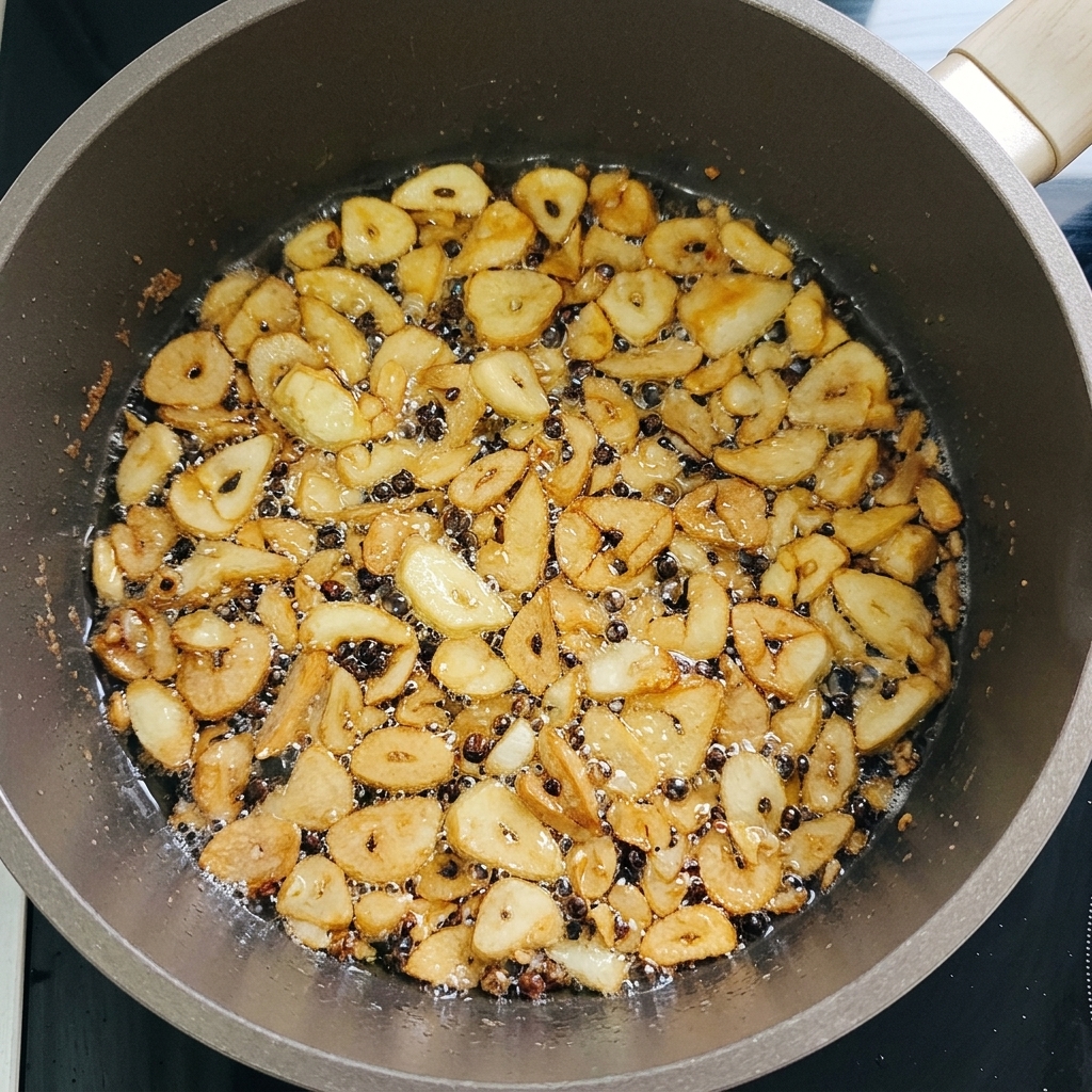 Finas láminas de ajo friéndose en una sartén con poco aceite, adquiriendo un color dorado crujiente.