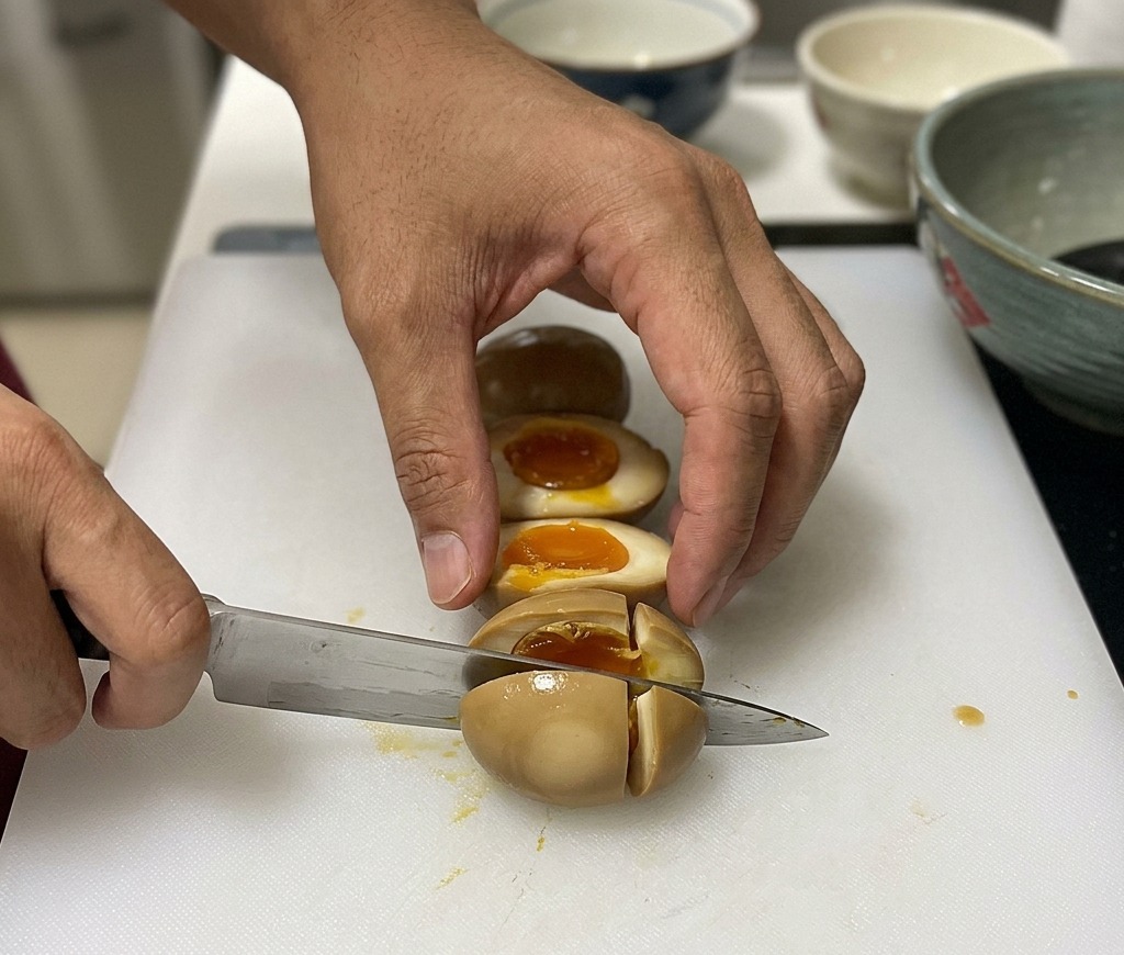 Chef cortando por la mitad un huevo mollet marinado de color marrón sobre una tabla de cortar, mostrando la yema naranja y líquida.