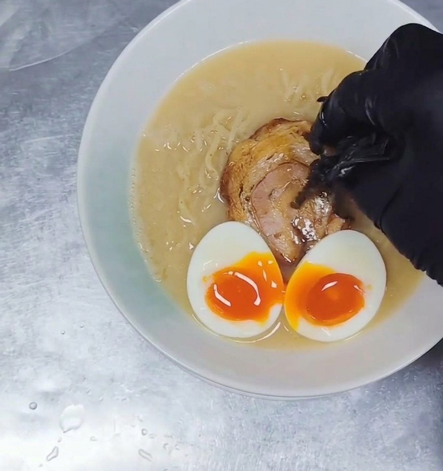 Tiras delgadas de setas oreja de judas oscuras siendo añadidas a un tazón de ramen completo con caldo, fideos, cerdo y huevos.