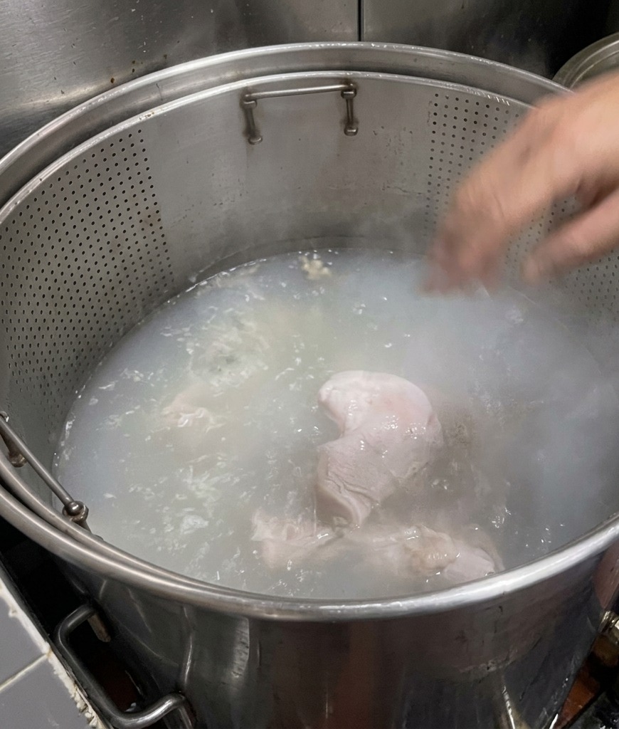 Trozos de huesos de cerdo sumergidos en una gran olla de agua hirviendo que pasa de transparente a un blanco lechoso.