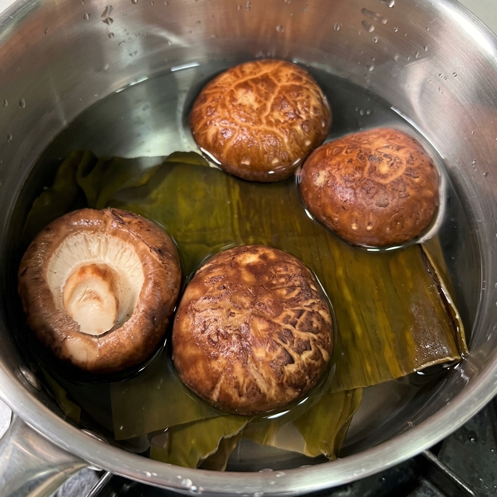 Alga kombu deshidratada y setas shiitake marrones remojándose en una olla pequeña con agua limpia.