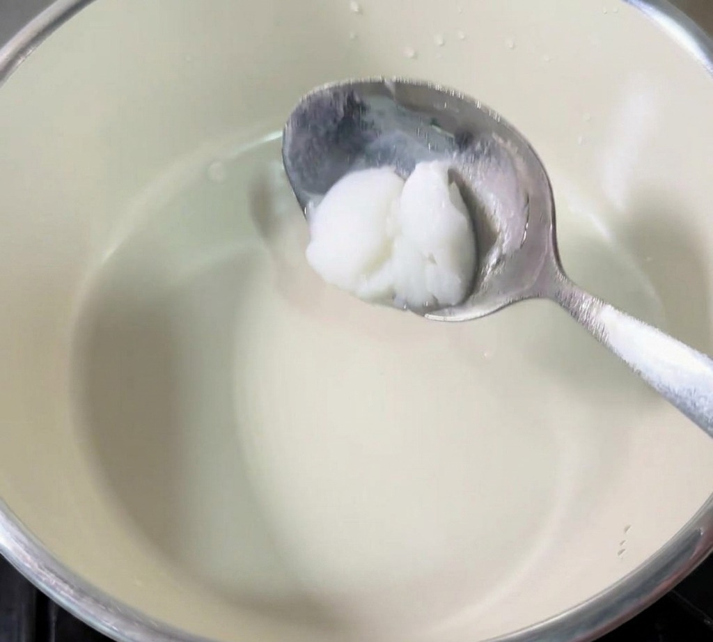 Una cuchara metálica sosteniendo una porción de manteca de cerdo blanca y sólida sobre el centro de un cazo pequeño.