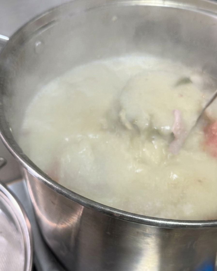 Caldo de cerdo blanco lechoso vertiéndose a través de un tamiz metálico en una olla con salsa oscura y manteca.