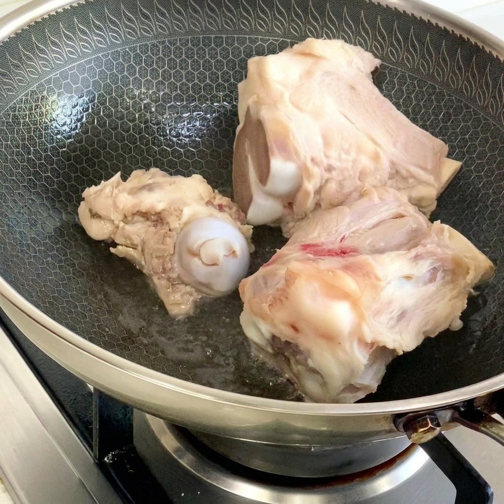 Huesos de cerdo sellándose en un wok con patrón de panal con una pequeña cantidad de aceite.