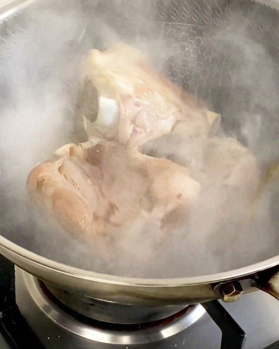 Huesos de cerdo en un wok de acero inoxidable envueltos en una espesa nube de vapor blanco tras añadir el vino para cocinar.