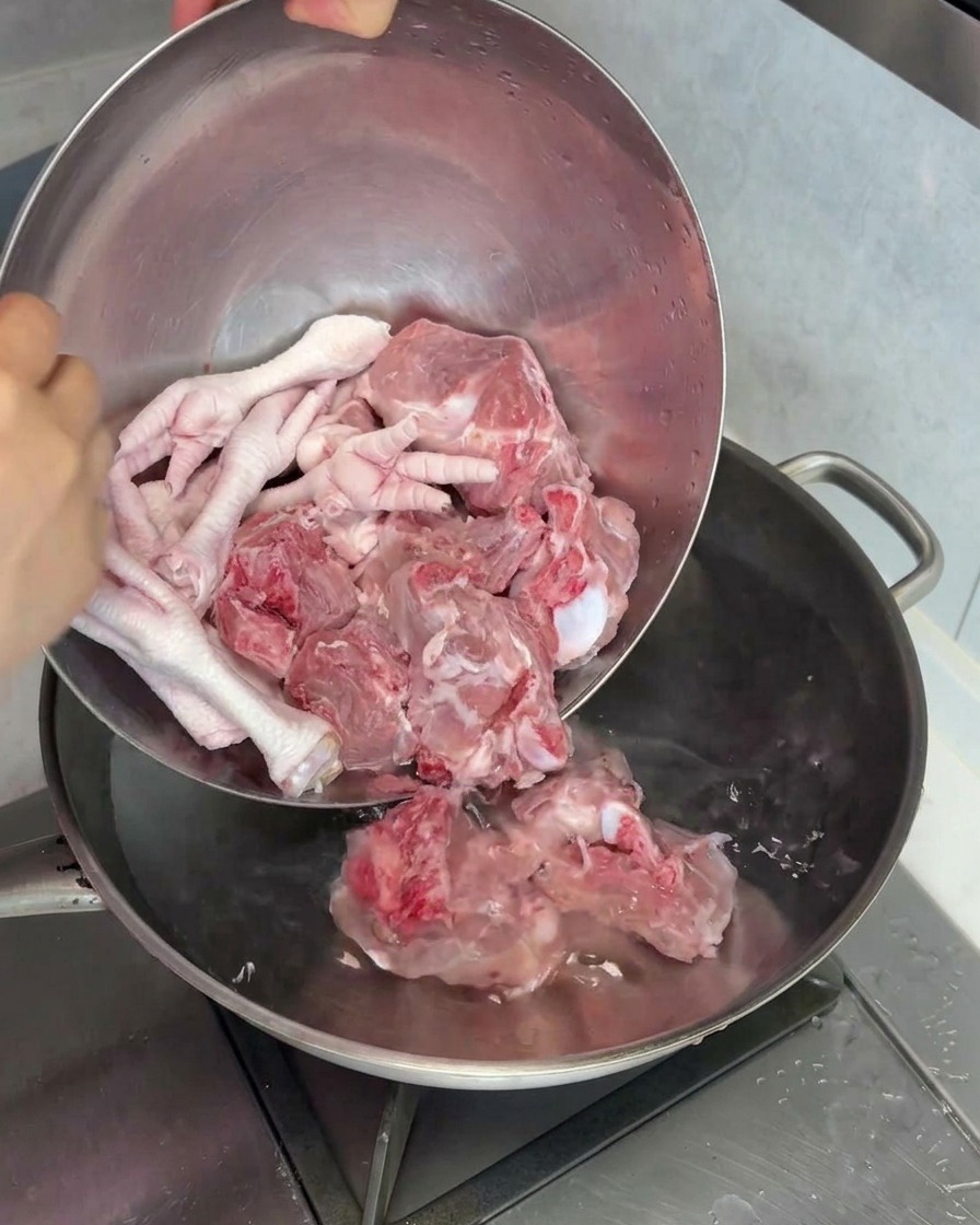 Huesos de tuétano de cerdo y patas de pollo crudas colocándose en una olla con agua para blanquearlos.