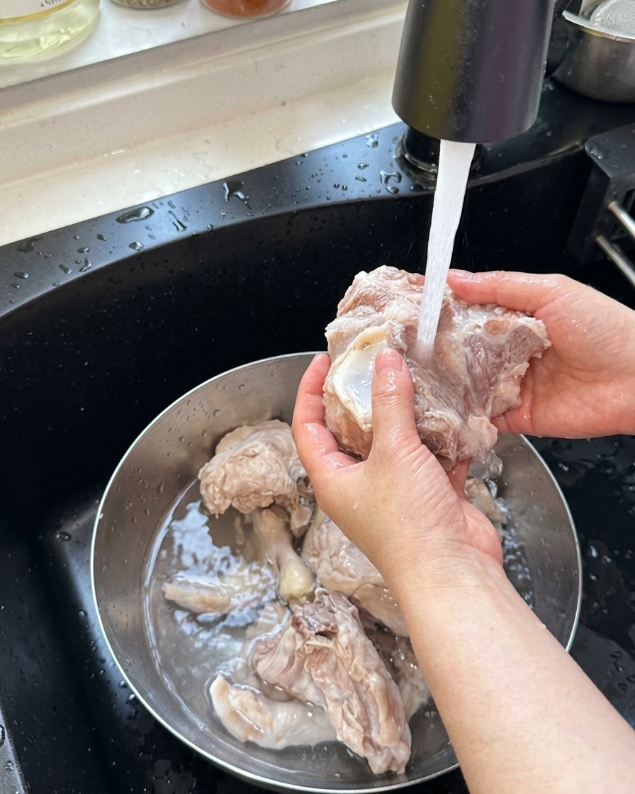 Huesos de cerdo y patas de pollo blanqueados enjuagándose bajo el grifo con agua tibia.