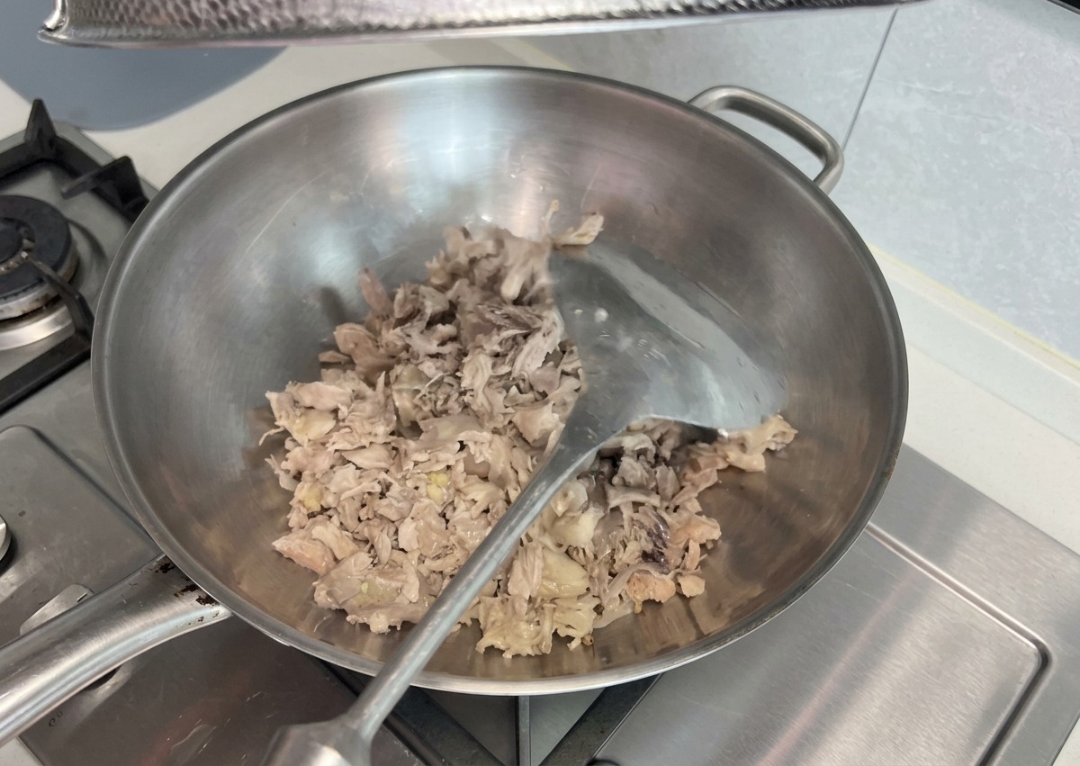 Restos de carne desmenuzada salteándose y machacándose con una espátula de metal en un wok grande.