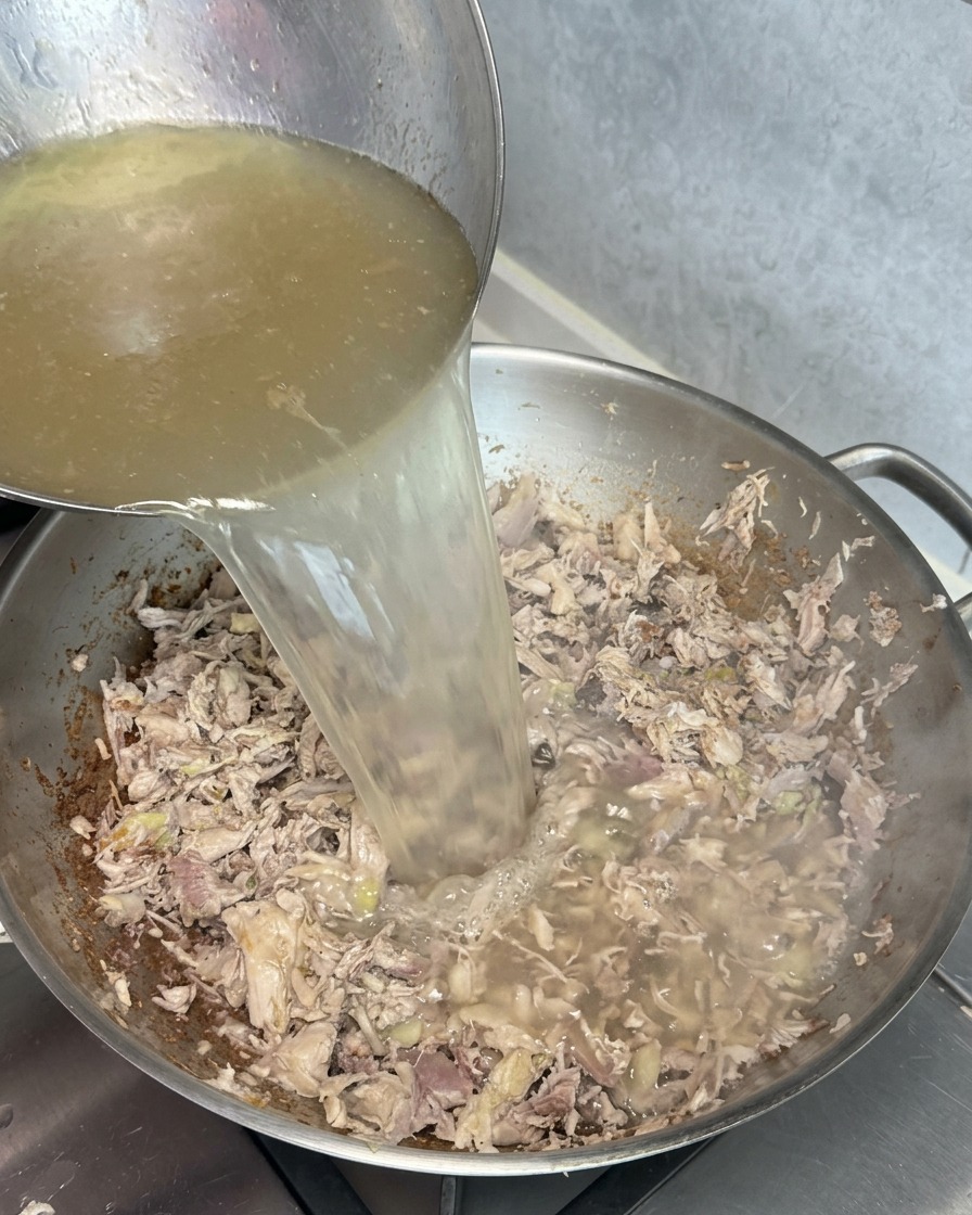 Un cucharón vertiendo caldo dorado en un wok con carne salteada, creando un líquido de aspecto turbio y blanquecino al instante.