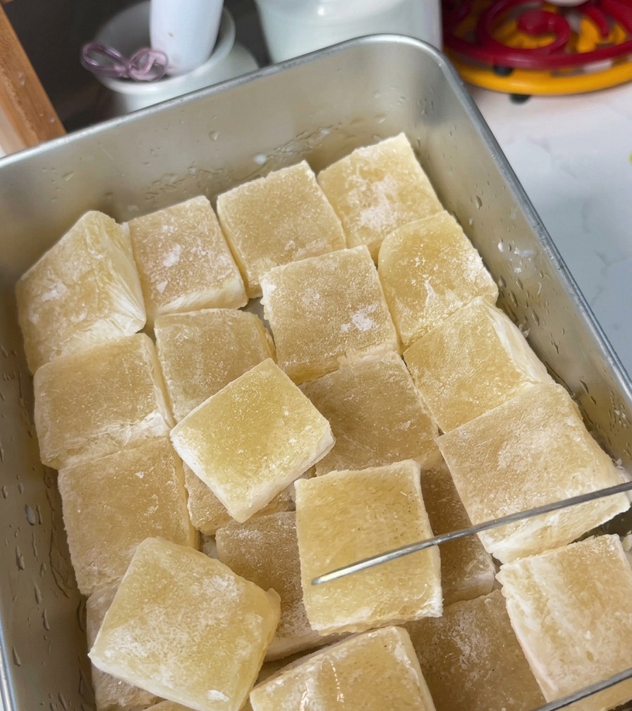 Gelatina de caldo amarillenta y traslúcida en una bandeja de metal cortándose en cuadrados.