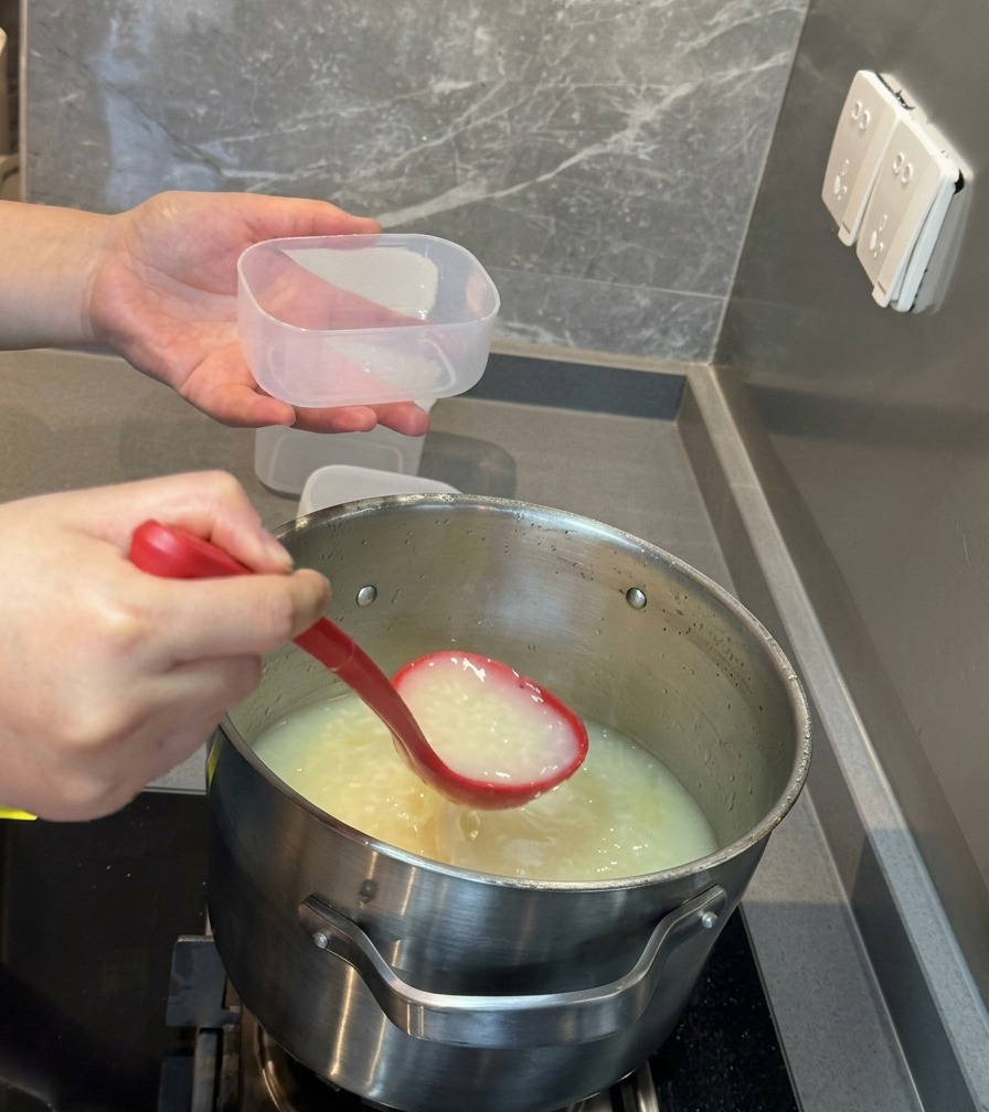 Un cucharón rojo vertiendo una rica sopa blanca de huesos de cerdo en un pequeño recipiente de plástico transparente para almacenar.
