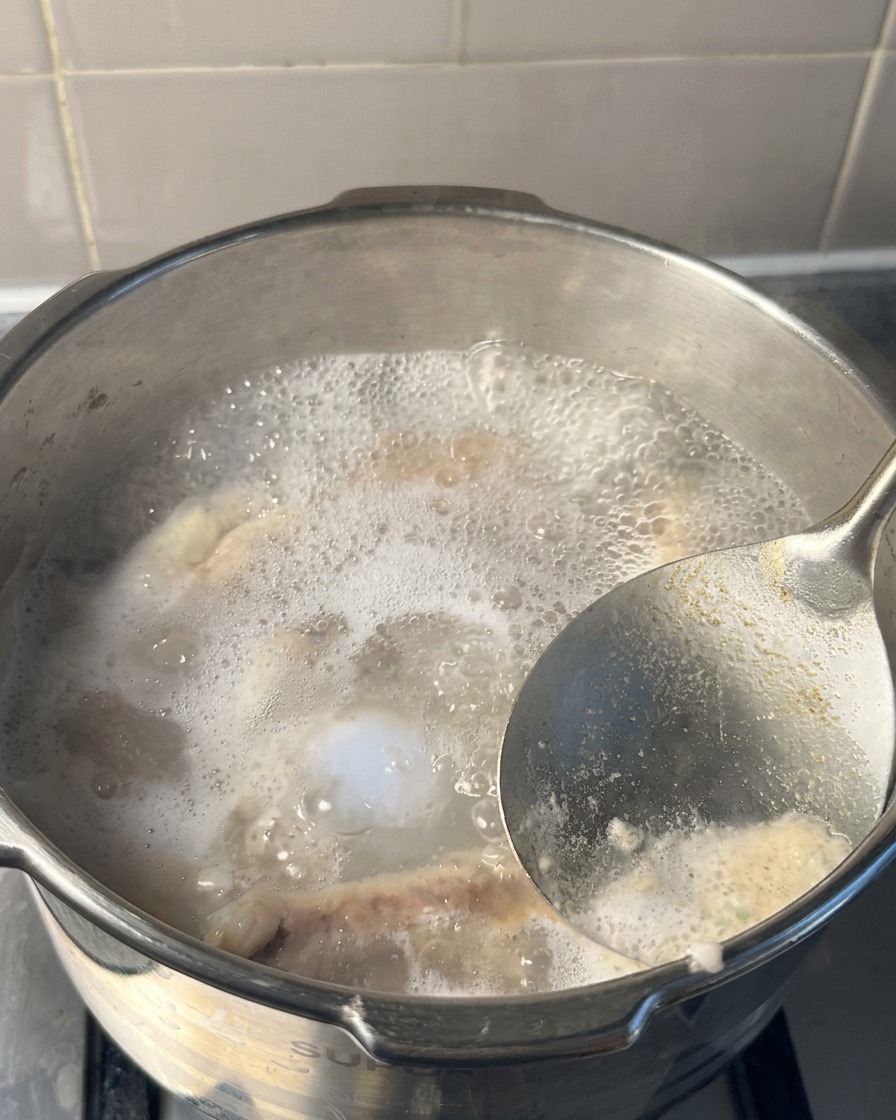 Un primer plano de un cucharón de metal retirando la espuma blanca y gris de la superficie del agua hirviendo dentro de una olla a presión.