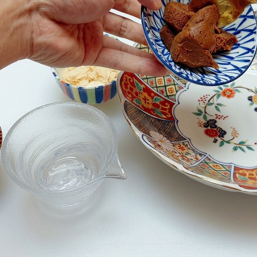 Una cuchara dorada sirviendo pasta de miso oscuro espesa en un tazón de porcelana con motivos azules y blancos.