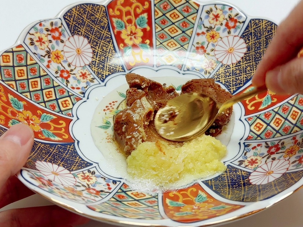 Una cuchara integrando varias pastas y condimentos en un colorido tazón de porcelana decorado.