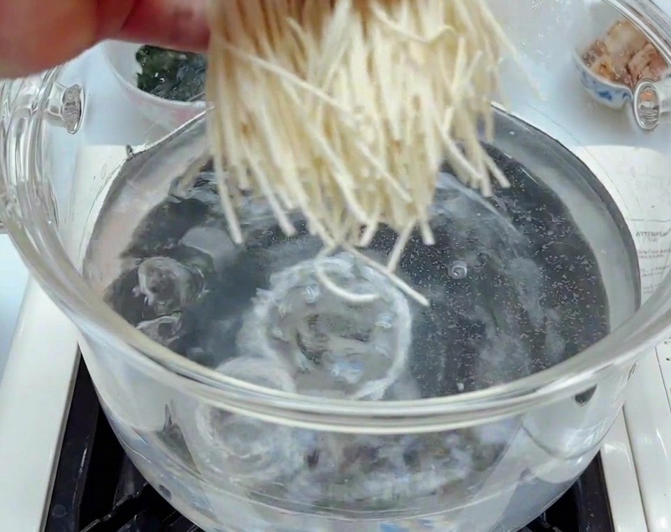 Fideos de ramen frescos de color blanco cayendo en una olla de vidrio transparente con agua hirviendo a borbotones.