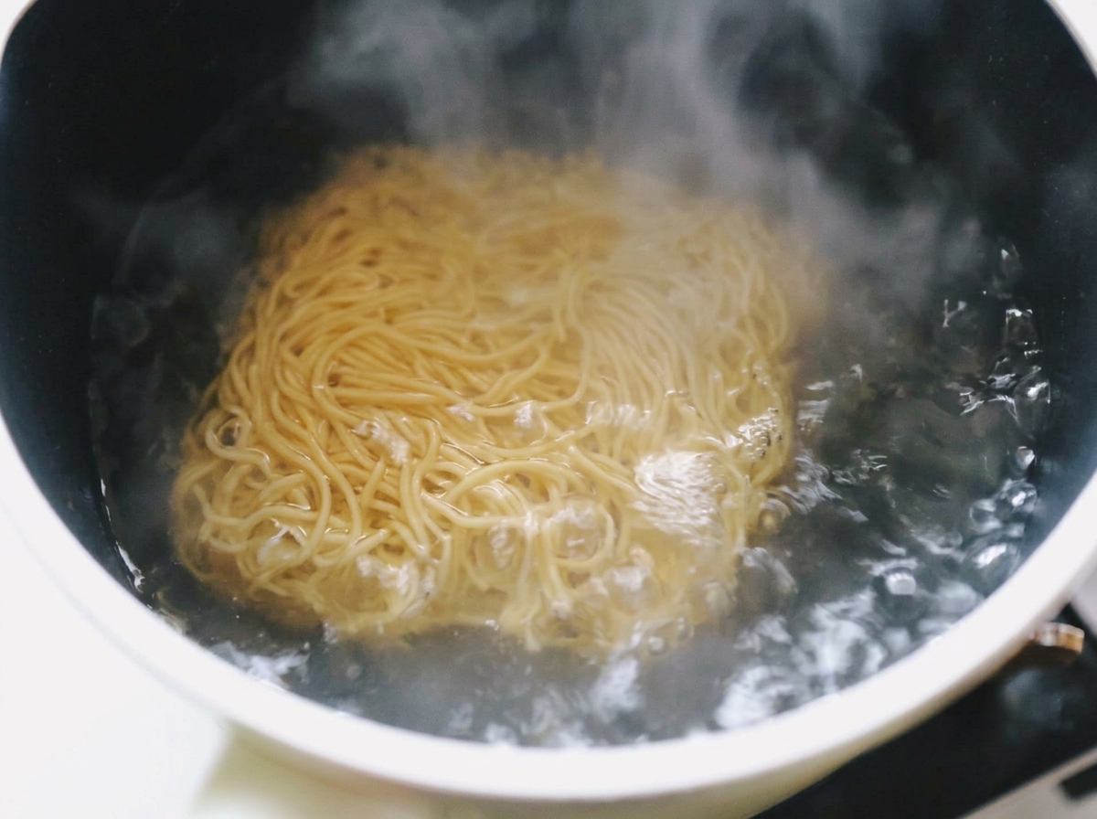 Fideos ramen instantáneos y ondulados sumergidos en una olla de agua hirviendo a borbotones con vapor subiendo.
