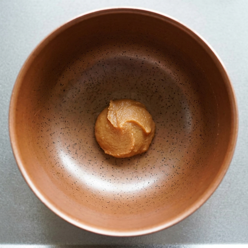 Una porción de pasta de miso espesa y marrón en el fondo de un tazón de cerámica moteado.