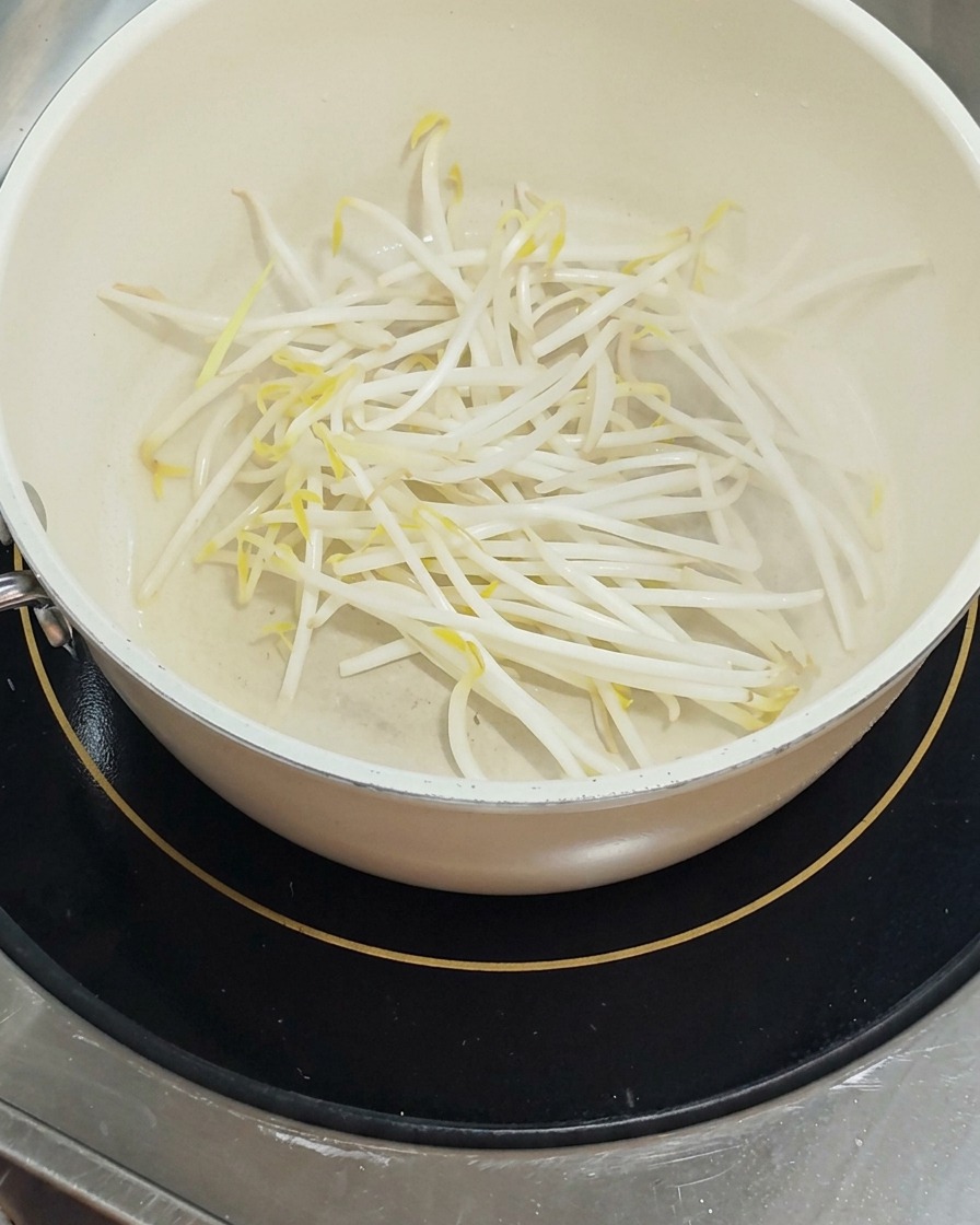 Un montón de brotes de soja frescos y blancos se encuentra en el fondo de una olla blanca, brillando ligeramente con el aceite.