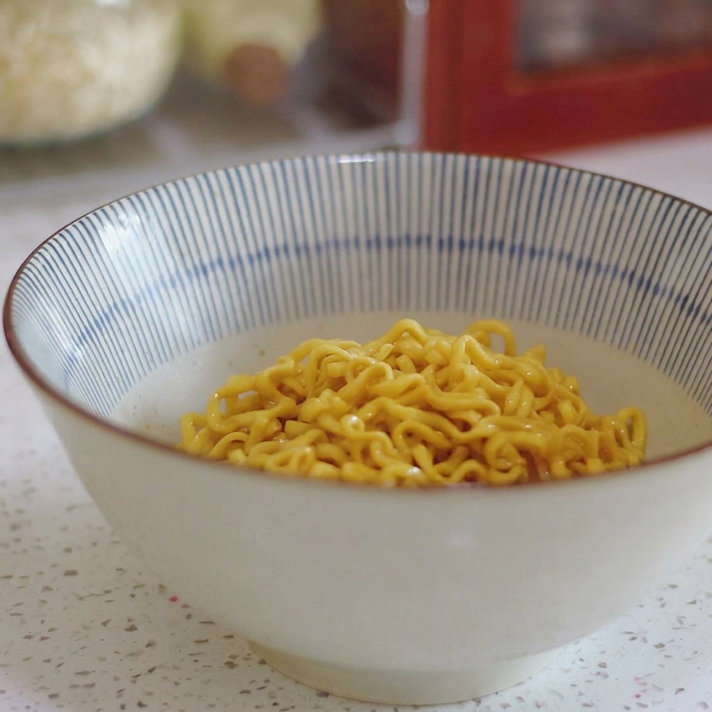 Fideos ramen rizados amarillos asentados en el fondo de un tazón de cerámica a rayas azules y blancas.
