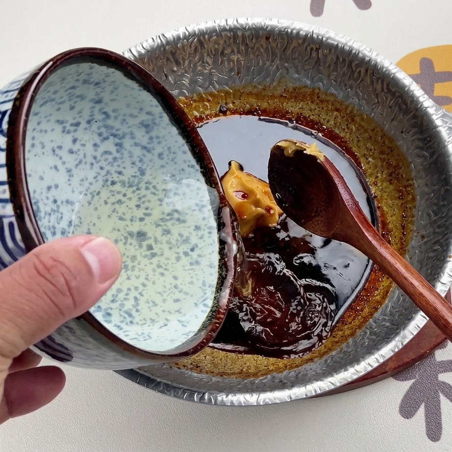 Caldo dashi claro vertiéndose desde un cuenco de cerámica con motivos azules y blancos sobre la salsa oscura de miso.