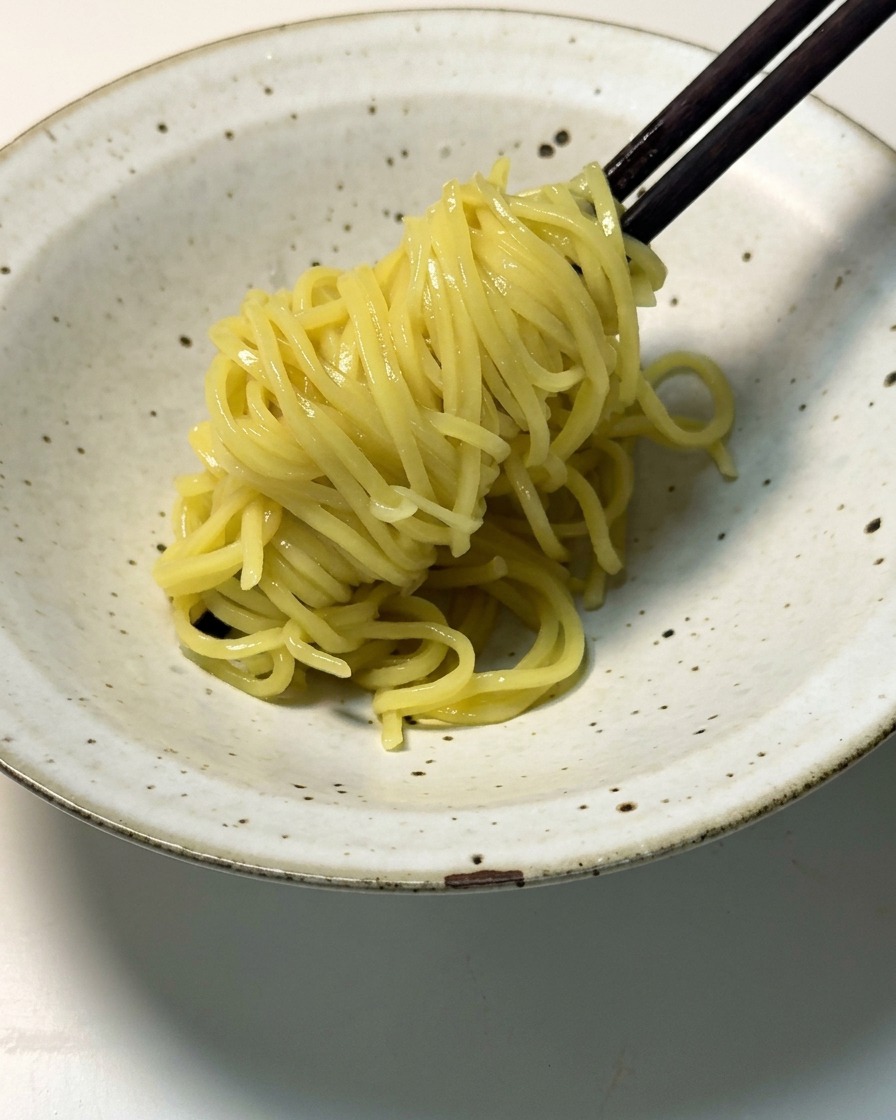 Fideos ramen amarillos cocidos levantándose con palillos de madera oscuros y colocándose en un cuenco de cerámica moteado y poco profundo.