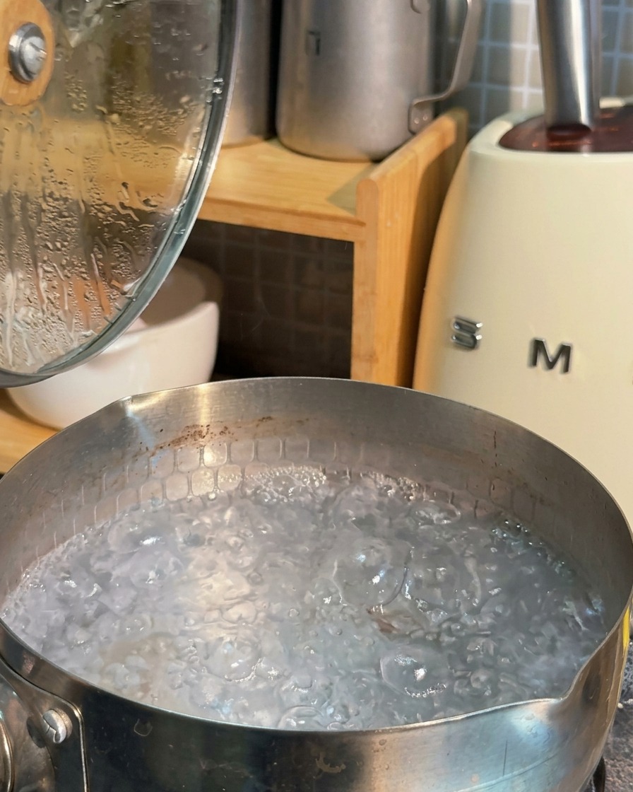 Una olla de acero inoxidable llena de agua hirviendo a borbotones con espuma blanca en la superficie.