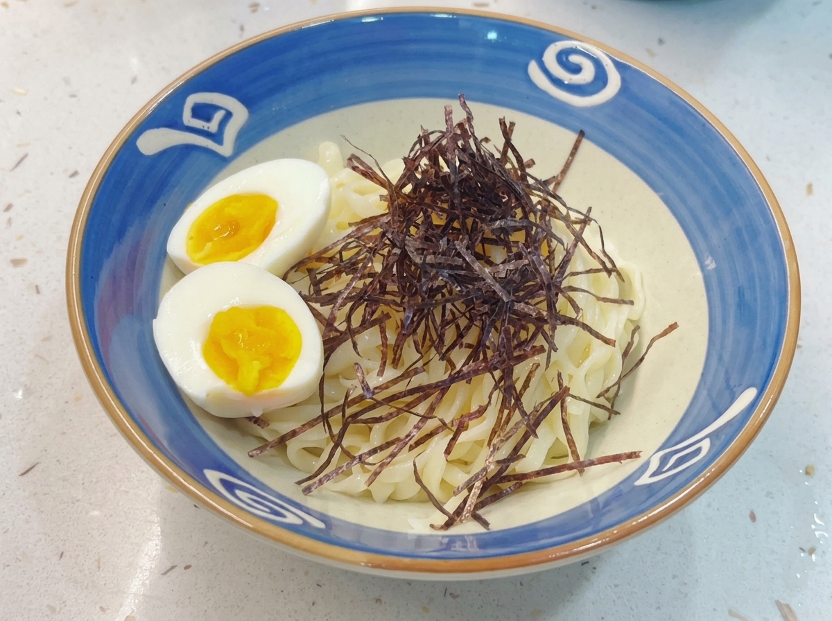Un bol terminado de fideos Tsukemen coronado con nori en tiras y rodajas de huevos cocidos con yema blanda.