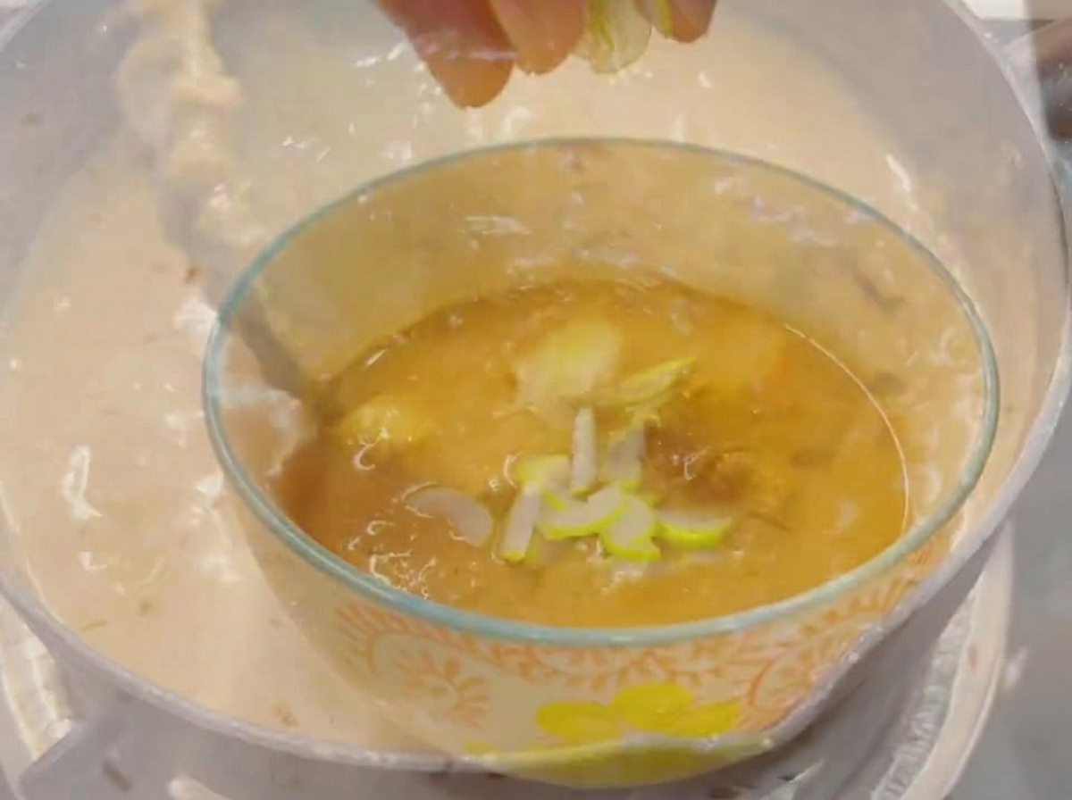 Puntas de los dedos dejando caer cebolletas verdes recién picadas en un pequeño bol de vidrio lleno de un caldo de inmersión espeso y sabroso.