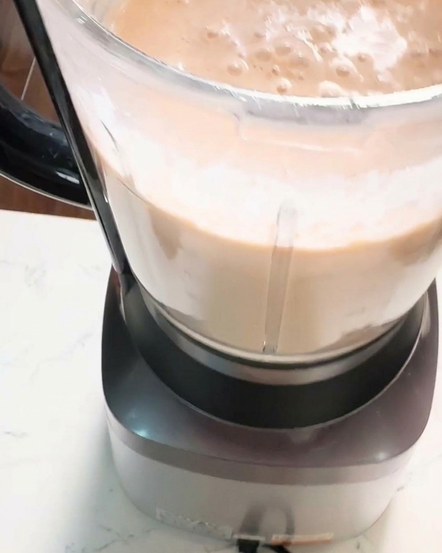 Un plano de cerca del vaso de una batidora de vaso lleno de una pasta de camarones espesa, suave y cremosa de color naranja rosado en pleno procesamiento.