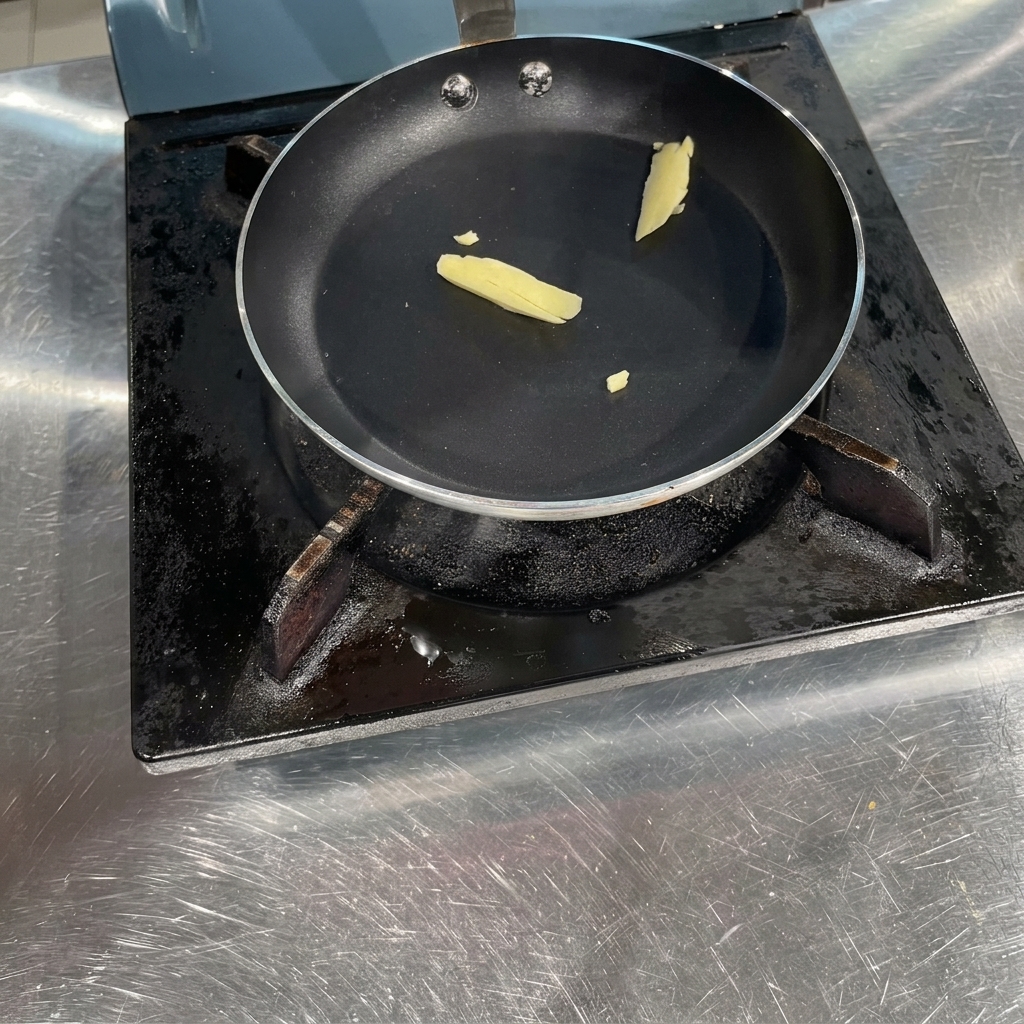 Un trozo pequeño de mantequilla amarilla derritiéndose en una sartén negra de fondo plano sobre la estufa.
