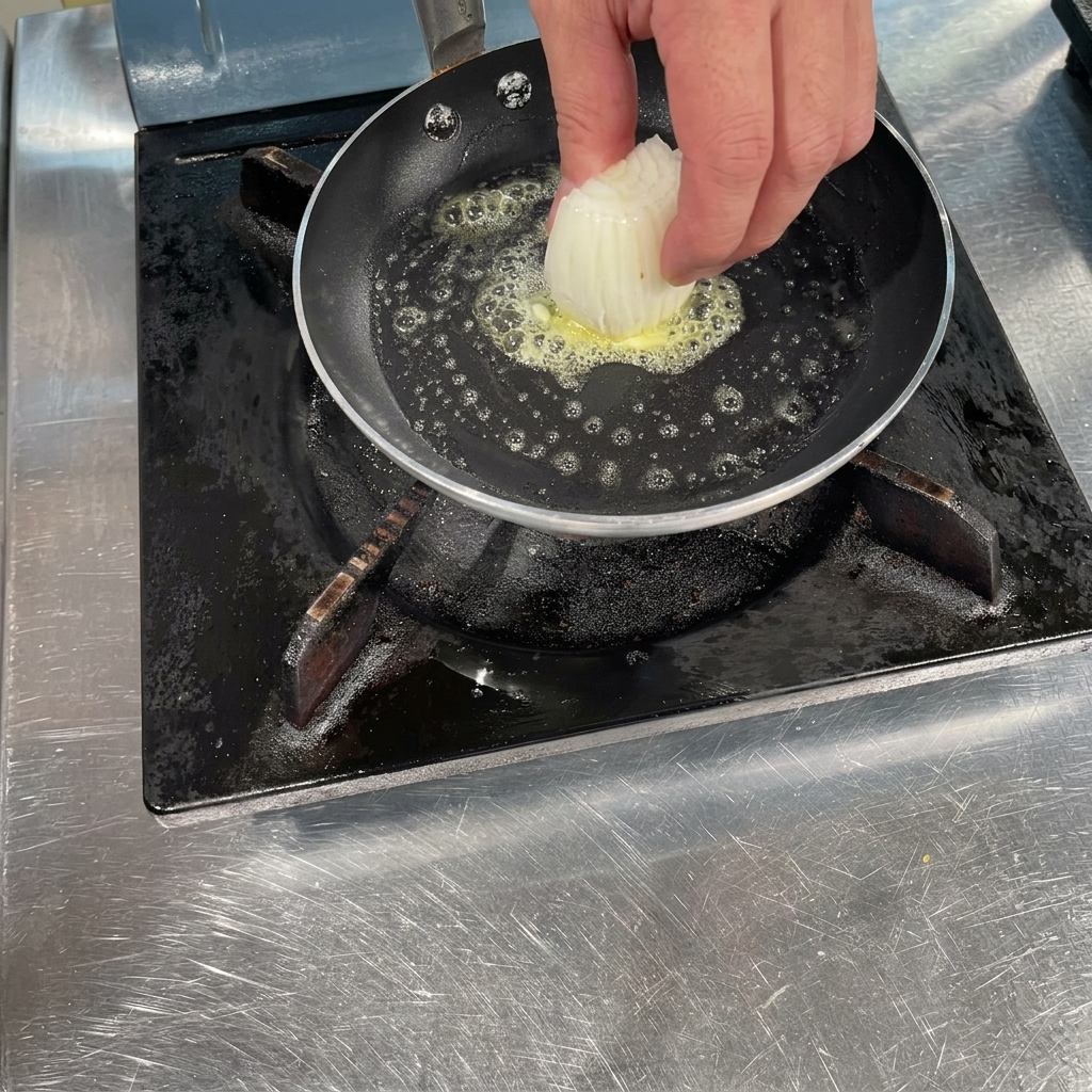 Una mano colocando un puñado de cebollas blancas picadas en una sartén caliente con mantequilla derretida burbujeando.