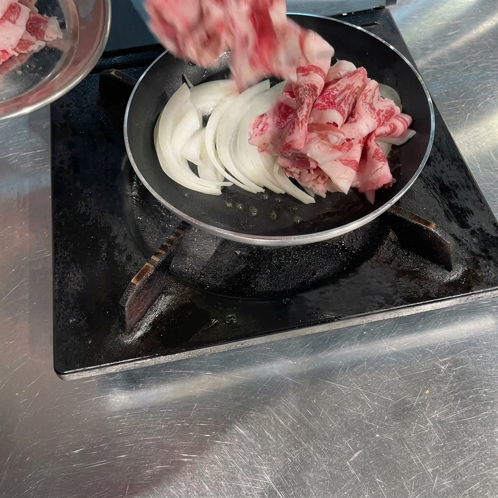 Rollos de carne de ternera cruda cortada muy fina siendo colocados en una sartén sobre cebollas blancas sofritas.