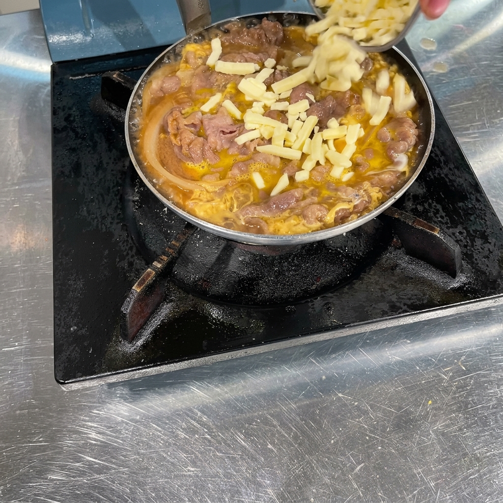 Una mano espolvoreando queso blanco rallado sobre una sartén llena de ternera cocinada, cebollas y huevo cuajado suavemente.