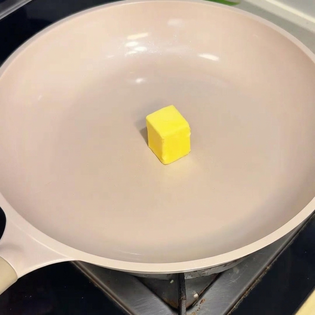 Un dado de mantequilla amarilla derritiéndose en una sartén antiadherente de color crema.