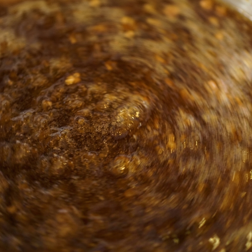 Primer plano de una salsa de color marrón oscuro burbujeando con fuerza en una olla mientras se remueve rápidamente.