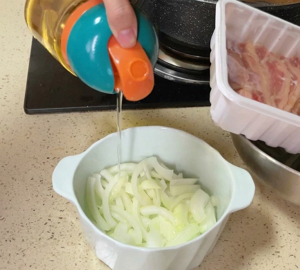 Un dispensador vertiendo aceite o sal sobre un tazón con cebolla cruda cortada en láminas en la encimera de la cocina.