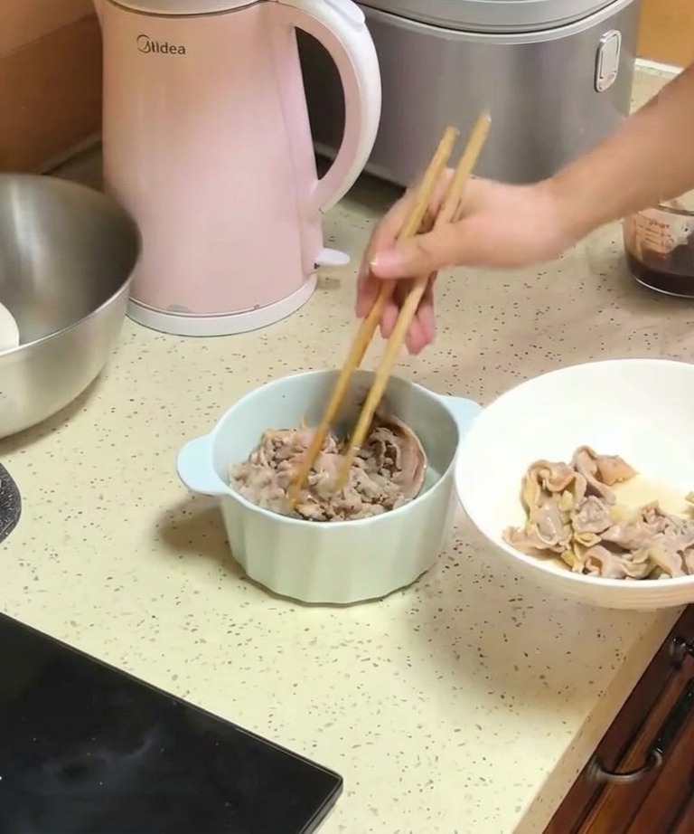 Una persona usando palillos de madera para pasar tiras de ternera escaldadas desde un plato blanco a un tazón con cebollas cocinadas.