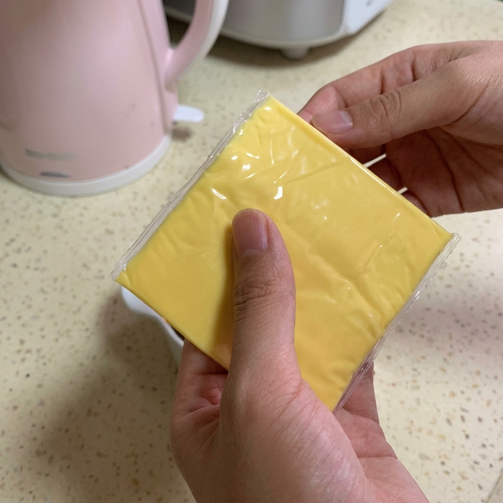 Una persona sosteniendo dos lonchas cuadradas de queso fundido de color amarillo brillante sobre un tazón lleno de ternera con salsa oscura.