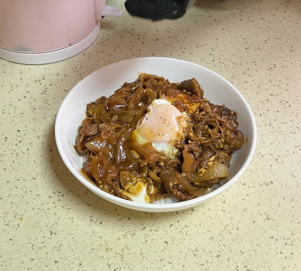 Una mano espolvoreando semillas de sésamo blanco y copos de perejil verde desde un recipiente sobre un tazón de arroz con ternera y huevo terminado.
