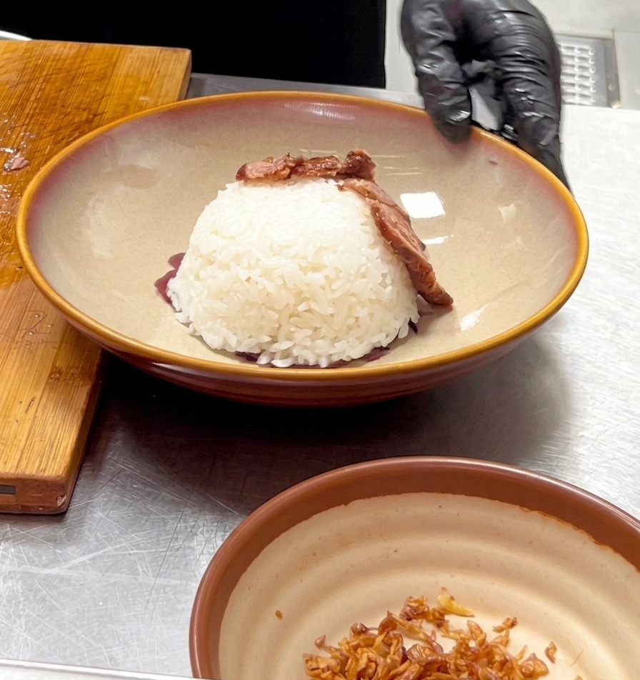 Una mano con guante colocando una tira de ternera cocinada sobre el domo de arroz blanco para darle forma de volcán.