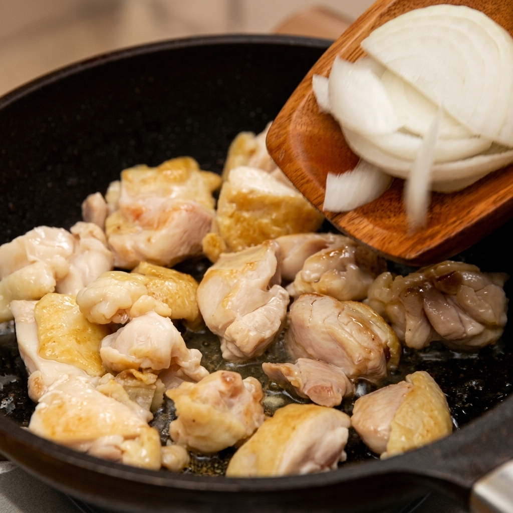 Cebolla blanca en rodajas finas pasándose desde una espátula de madera hacia la sartén con el pollo salteado.