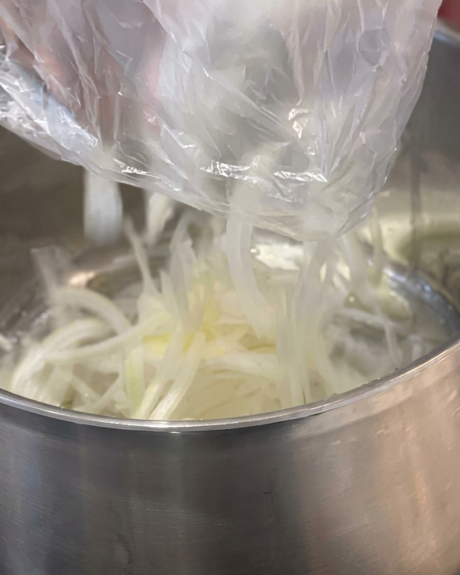 Tiras de cebolla blanca cayendo en una olla de acero inoxidable junto a un trozo de mantequilla amarilla.